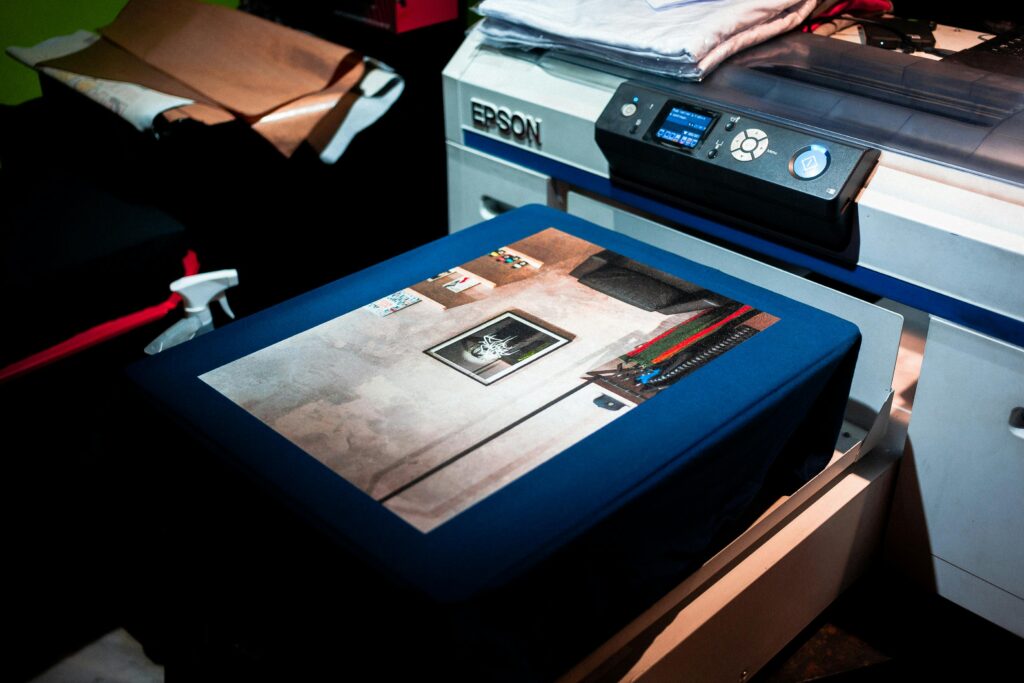 pexels photo 5727002 5727002 Close-up of a professional printer printing a custom artwork design on fabric in a studio setting.
